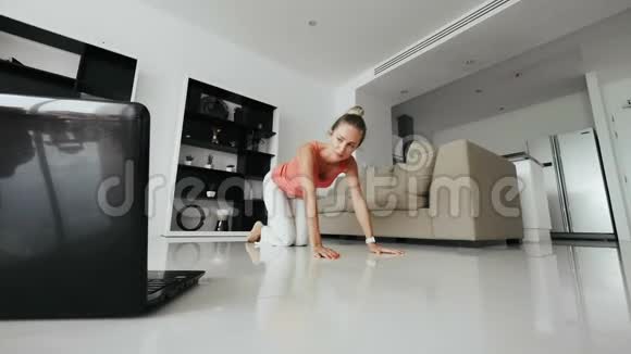 家庭主妇看着手提电脑在家里的地板上做健身运动视频的预览图