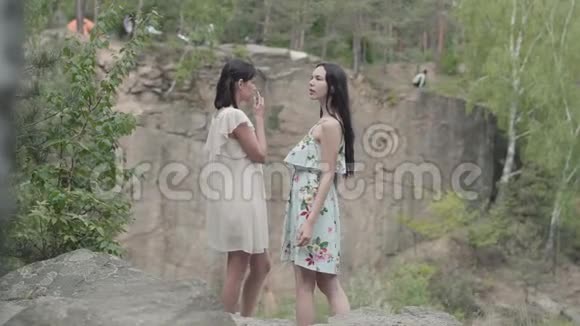 两个穿着短裙的美女站在岩石上开着野花看着森林视频的预览图