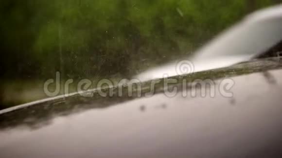从外面看有大雨阵雨水滴落在站在停车场的空黑车的车篷上视频的预览图