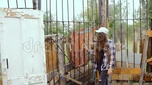 一个年轻的女人沿着铁栅栏走旧木门被绑在那里视频的预览图
