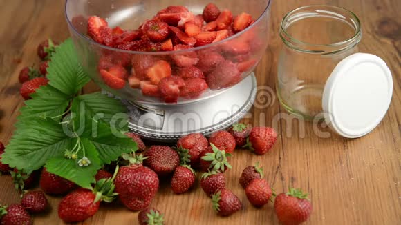 在碗里放草莓重量和糖木桌上的叶子和花头果酱制作视频的预览图