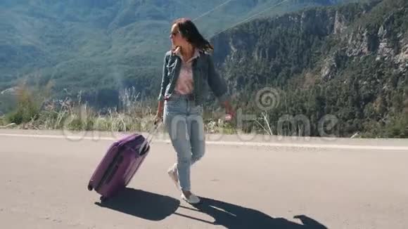 美丽的年轻女士在农村的道路上带着手提箱搭便车在阳光明媚的日子户外视频的预览图
