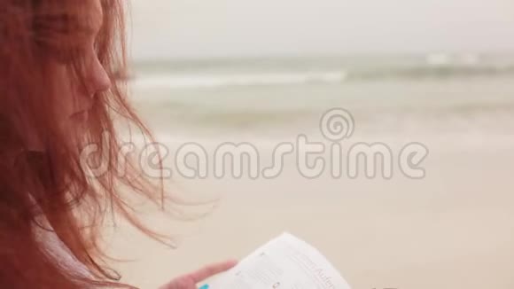 海滨的红发女孩翻阅着书视频的预览图