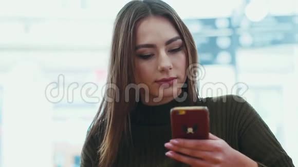 漂亮的年轻女人穿着时尚的服装通过手机发短信坐在咖啡馆A时微笑玩得开心视频的预览图