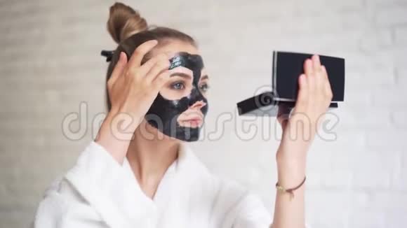 笑的年轻女孩头上戴着一条毛巾脸上戴着一个黑色的面具日间水疗中心视频的预览图