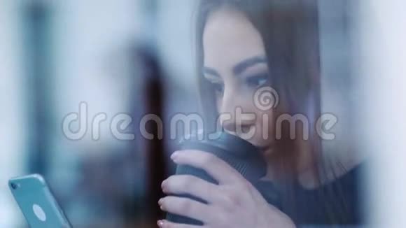 一个迷人的女孩坐在窗户旁用她的手机喝咖啡浪漫气氛视频的预览图