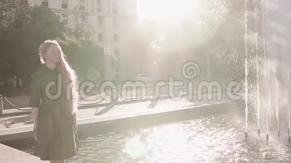年轻漂亮的红发女郎穿着绿色衣服走在喷泉旁视频的预览图