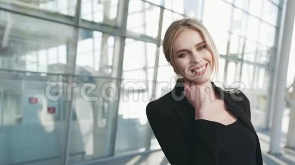 穿着黑色衣服的漂亮金发女人看着镜头露出美丽的微笑机场航站楼视频的预览图