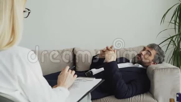 躺在沙发上的男人在办公室里和专业的心理治疗师或心理学家谈论他的问题视频的预览图