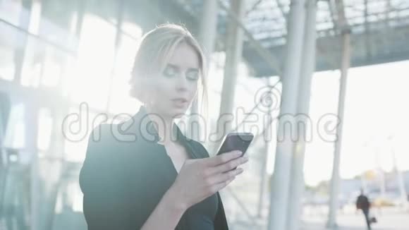 一位身穿黑色正式服装的金发美女站在机场门口用手机发短信视频的预览图