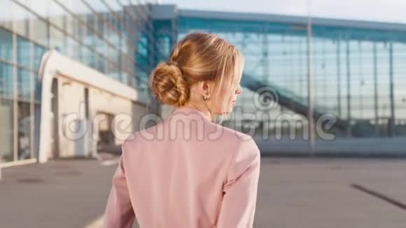 一位穿着时髦衣服的优雅年轻女子在机场入口处匆忙行走转向照相机后景视频的预览图