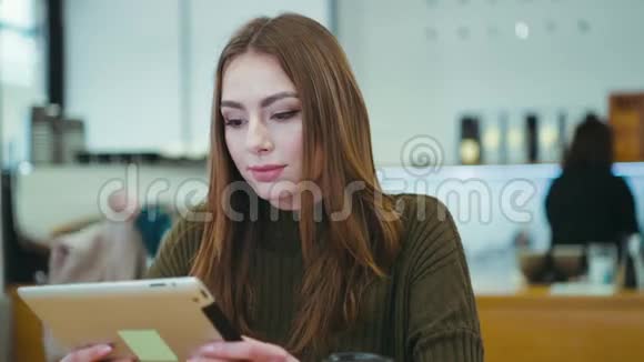 漂亮的黑发女孩穿着时髦的休闲装独自坐在咖啡馆里用平板电脑得到信息反应视频的预览图