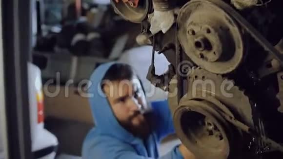 有胡子的汽车机械师坐着从下面的螺丝螺栓进入电机的身体挂在链条上视频的预览图