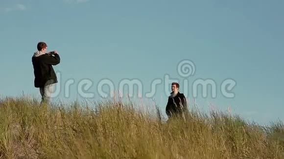 两个年轻人站在高高的草地上其中一个正在用手机拍照视频的预览图