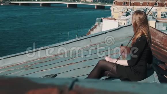 可爱的小女孩穿着黑色连衣裙坐在屋顶与风景优美的城市景观视频的预览图