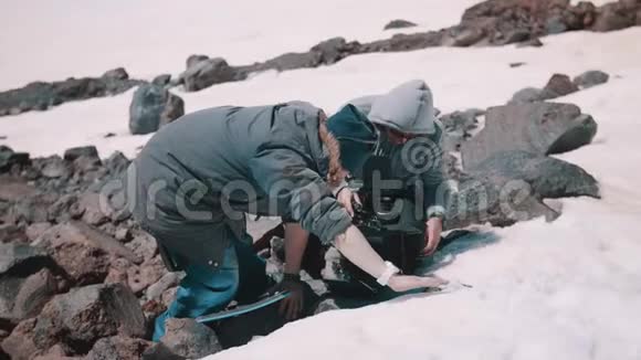 两名拍摄人员在雪山悬崖的防水垫上放置摄像机视频的预览图