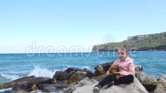 小女孩和她可爱的小狗坐在岩石上视频的预览图