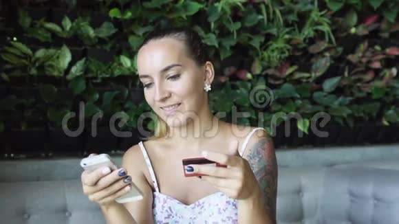 有纹身的漂亮女人用信用卡和手机买新衣服视频的预览图