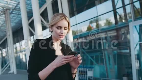 漂亮的金发女商人化妆自然走在商务中心在她的电话短信视频的预览图