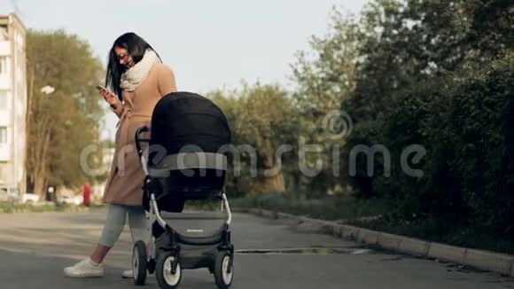一个年轻的女孩带着婴儿车穿过公园在电话里交谈视频的预览图