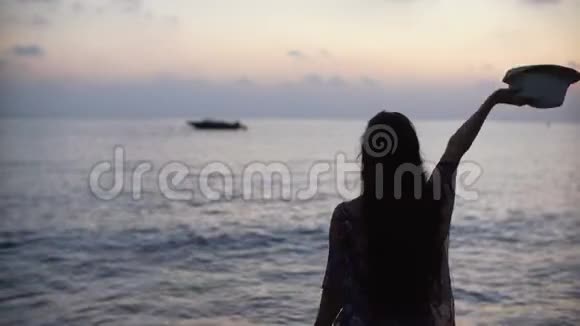 日落时分一位留着长发的年轻女子在海上挥舞着帽子视频的预览图