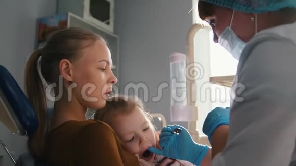 牙医检查和咨询坐在母亲膝盖上的女儿视频的预览图