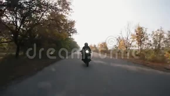 一位身穿黑色头盔和皮夹克的男子骑摩托车在乡间小路上的正面景色视频的预览图