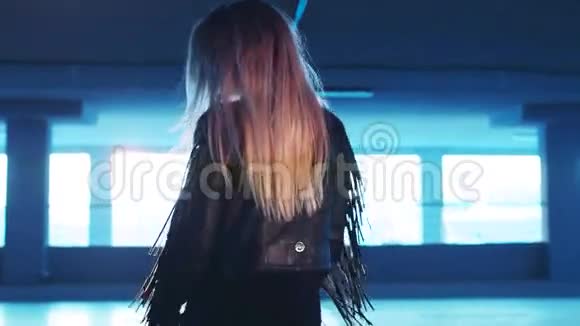 一个穿着波霍式皮夹克的长发年轻女孩从停车场走下来转向照相机从后面看视频的预览图