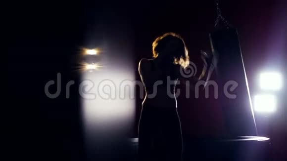 年轻女子在黑暗中拳击女性剪影做暗箱操作她身后的强光视频的预览图