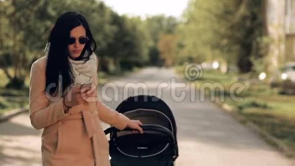 一个年轻的女孩带着婴儿车穿过公园在电话里交谈视频的预览图