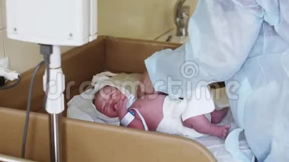 在妇产医院护士穿着浴袍用蓝色手镯包裹新生儿视频的预览图