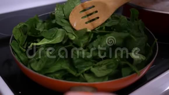 在热炉炉顶上用平底锅搅拌萎蔫的菠菜视频的预览图