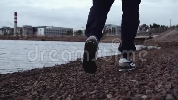 穿着时髦运动鞋的人的腿在城市的岩石海岸上行走视频的预览图