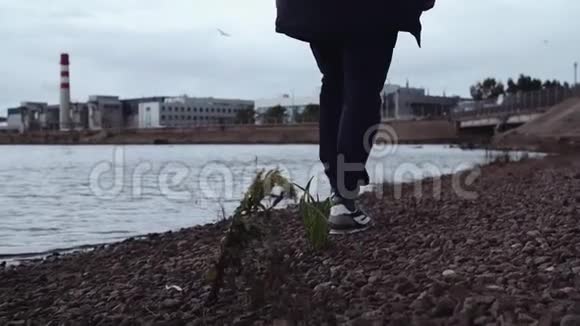 穿着时髦运动鞋在城市岩石海岸行走的人的腿视频的预览图