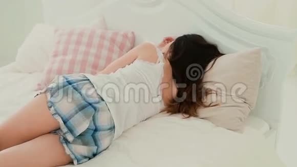 穿着睡衣躺在床上的年轻女子困倦的女孩放松早上在家休息慢动作视频的预览图