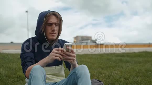 休闲快乐的男人用智能手机坐在草地上的公园学生的长凳上视频的预览图
