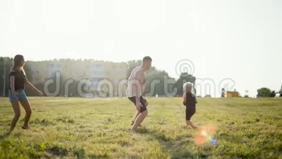 幸福的年轻家庭正在和小孩子在美丽的日落草地上打球视频的预览图
