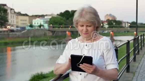 傍晚时分在海滨老城区河边河边使用带有耳机的平板电脑视频的预览图