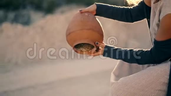 穿着民族服装的女孩坐在路边从水罐里倒出沙子水变成了沙子视频的预览图