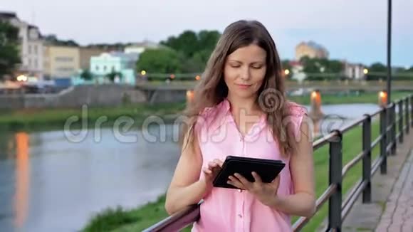 傍晚时分在海滨旧城河桥的栏杆旁使用平板电脑的漂亮少女视频的预览图