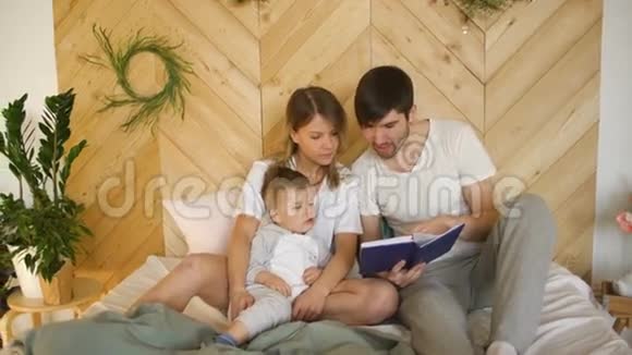 可爱的三口之家躺在床上家庭拥抱和读书视频的预览图
