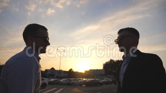 两个年轻的商人站在户外靠近停车场和交谈商人们在城外与视频的预览图