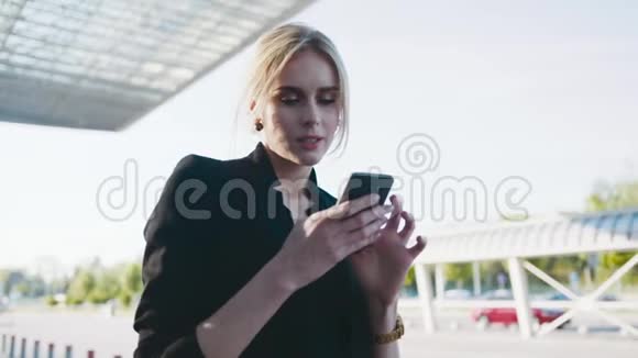 旋转近距离观看一个漂亮的金发女人站在机场候机楼旁等待着某人并使用她视频的预览图