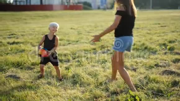 幸福的年轻一家人在美丽的夕阳下和小男孩在草地上玩球视频的预览图