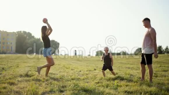 幸福的年轻一家人在美丽的夕阳下和小男孩在草地上玩球视频的预览图