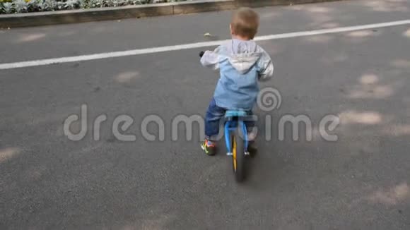 慢动作4k一个孩子在公园里骑跑步自行车一个小男孩在城市公共公园里骑平衡自行车视频的预览图