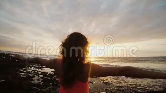 海滩上的年轻女子看着美丽的日落女看天涯风吹发喜欢海景视频的预览图