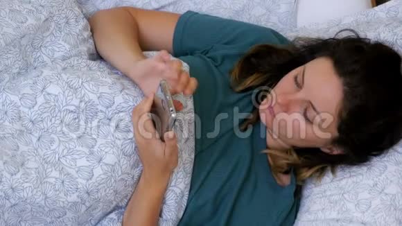 早上躺在一张白色床上的女人使用智能手机的俯视图视频的预览图