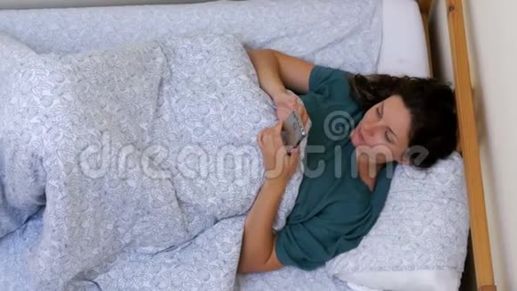 早上躺在一张白色床上的女人使用智能手机的俯视图视频的预览图