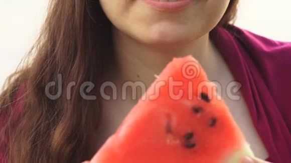 年轻女子在池塘的背景上吃一块红色多汁的西瓜视频的预览图
